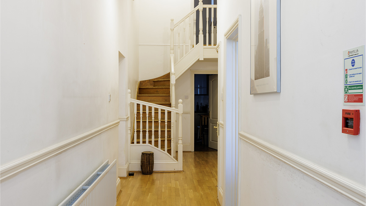 Before image of a traditional London flat hallway with wooden staircase and white banisters, prior to modern interior design updates