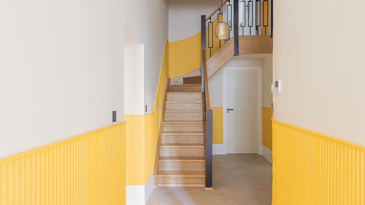 After image of a beautifully renovated London flat staircase with wooden steps, black railing, and vibrant yellow fluted wall panels